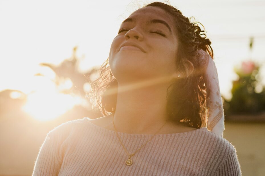 Mulher jovem de olhos fechados sorrindo ao pôr do sol, simbolizando amor próprio, autoestima feminina e o ato de se priorizar sem culpa