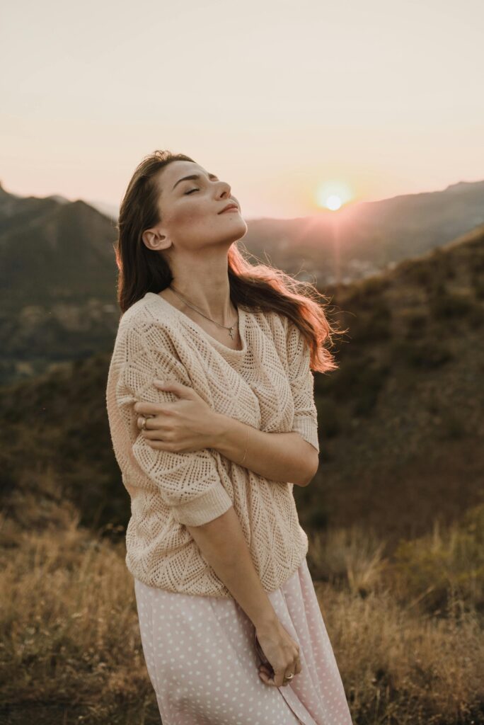 Mulher de olhos fechados ao pôr do sol abraçando a si mesma — amor próprio
