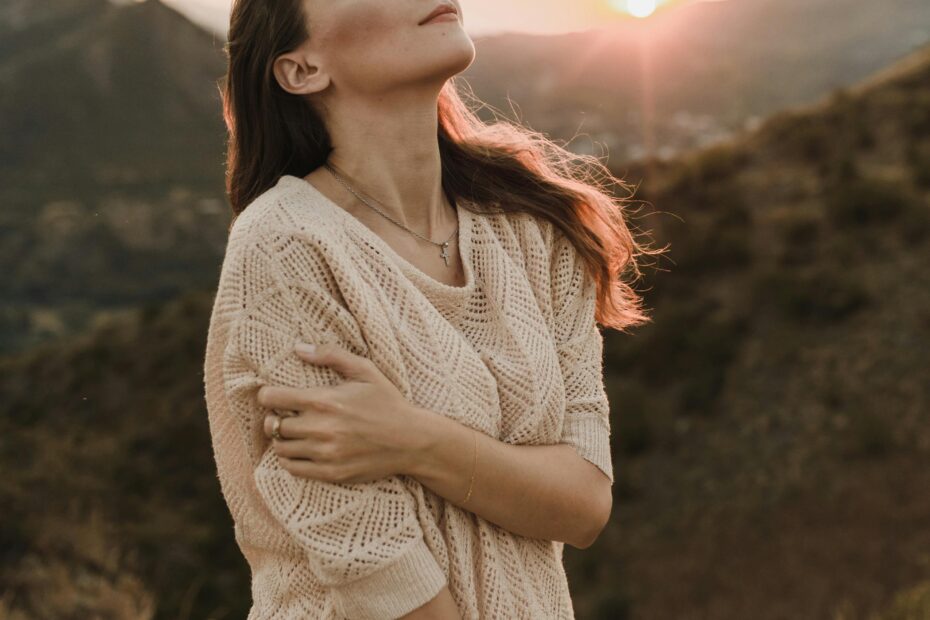 Mulher de olhos fechados ao pôr do sol abraçando a si mesma — amor próprio